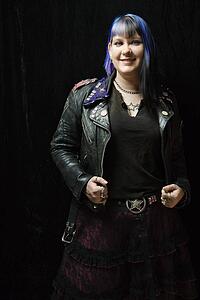 Portrait of smiling Caucasian woman with blue hair and black leather jacket standing against black background.