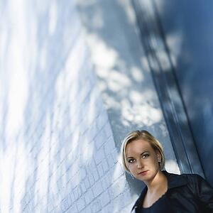 Blonde woman standing against sun dappled building looking at viewer