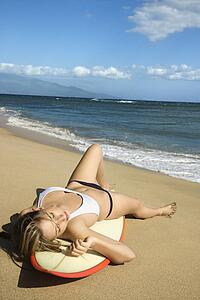 Sexy young Caucasian woman in bikini lying on surfboard sunbathing at beach 