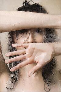 Pretty Caucasian young woman wet in shower leaning against glass.