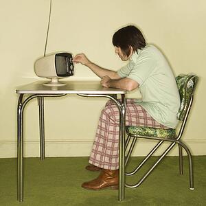 Side view of Caucasian mid-adult man sitting at 50's retro dinette set turning old television knob.
