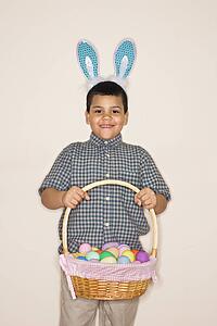 Boy wearing bunny ears holding Easter basket smiling