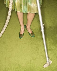 Close-up of Caucasian female legs with vacuum extension against green retro carpet.