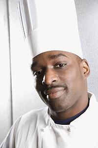 Head shot of African-American male chef wearing traditional uniform and toque looking at viewer.