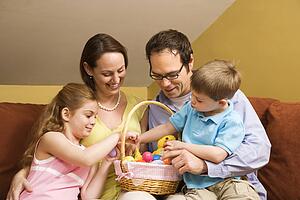 Caucasian family on couch looking at Easter basket. 