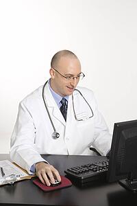 Caucasian mid adult male physician sitting at desk with laptop computer.