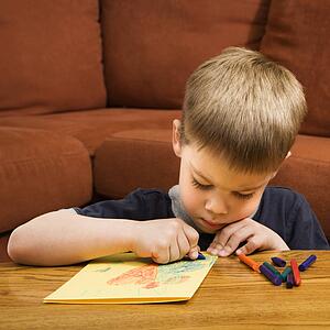 Caucasian boy drawing on yellow paper with crayons.