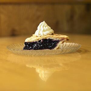 Slice of blueberry pie on plate with whipped topping