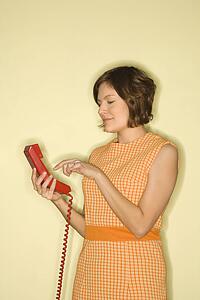 Pretty Caucasian mid-adult woman wearing orange dress standing dialing red telephone.