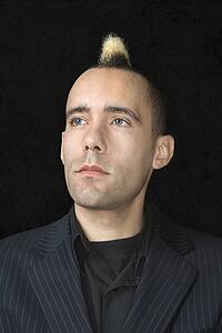 Portrait of Caucasian man in suit with mohawk against black background.