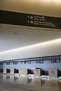Signs for terminal and gates with empty check-in station in background at airport.