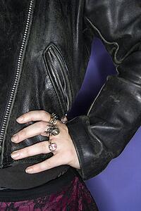 Caucasian woman's hand on hip wearing silver rings and black leather jacket.