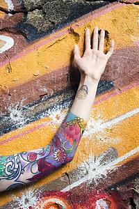 Tattooed woman's arm against graffiti covered wall