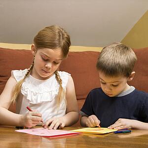 Caucasian boy and girl drawing on paper with crayons.