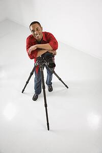 Young African American male adult photographer posing with camera and tripod.