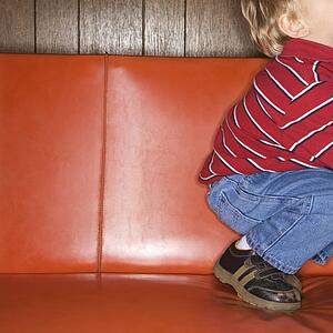 Caucasian boy kneeling on vinyl sofa.