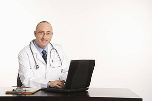 Caucasian mid adult male physician sitting at desk with laptop computer.