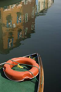 Boat with reflection of buildings in water in background