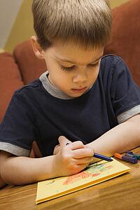 Caucasian boy drawing on yellow paper with crayons.