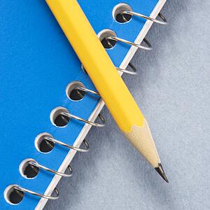 Sharp pencil placed on blue spiral bound notebook.