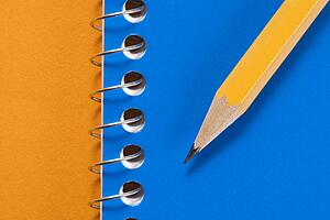 Sharp pencil placed on blue spiral bound notebook