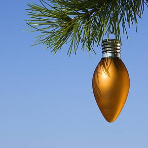 Orange ornament hanging on Christmas tree branch against blue background.