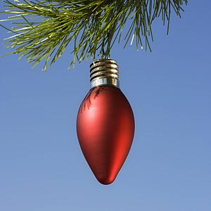 Red ornament hanging on Christmas tree branch against blue background.