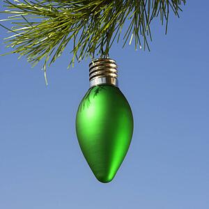 Green ornament hanging on Christmas tree branch against blue background.
