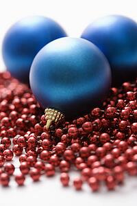 Still life of large blue Christmas ornaments and strings of red beads.