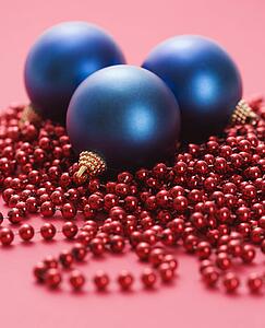 Still life of large blue Christmas ornaments and strings of red beads on red background.