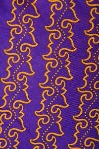 Close-up of purple vintage fabric with repetitive orange designs printed on polyester