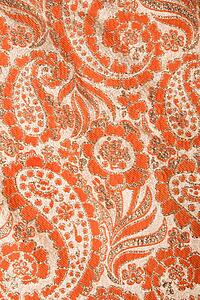 Close-up of orange textural vintage fabric with paisley and metallic thread stitching