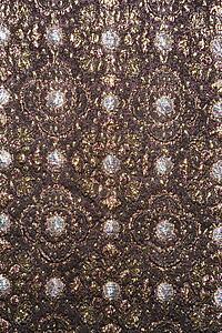 Close-up of textural vintage fabric with repetitive shapes and metallic thread stitching