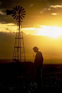 Silhouette of a man standing in front of a rural windmill