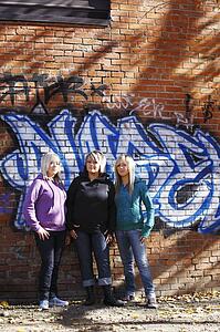 Three teens standing in front of graffiti
