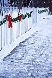 Christmas garland and red bows on a white picket fence
