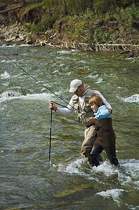 Father and son crossing a mountain fly fishing river 