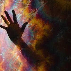 Female hand silhouetted behind tye-dye fabric.