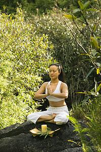 Woman sitting on boulder in forest meditating with candle