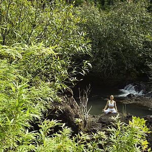 Woman sitting on boulder by creek meditating