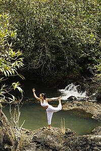 Woman doing yoga balancing on boulder by creek in Maui, Hawaii
