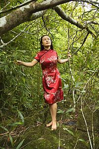 Portrait of Asian American woman in ethnic attire standing on rock in bamboo in Maui, Hawaii.