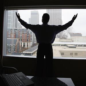 Male with raised arms in office with skyline in background