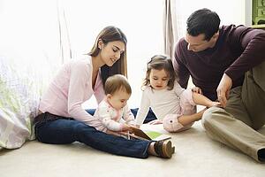 Children with parents sitting on bedroom floor looking at book