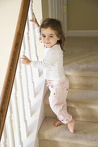 Girl standing on carpeted stairs holding onto railing