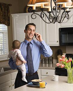 Father in holding baby and talking on cellphone in kitchen