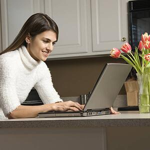 Woman in kitchen looking at laptop computer