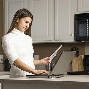 Woman in kitchen looking at laptop computer
