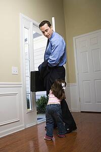 Businessman at open door with briefcase with daughter tugging on his leg