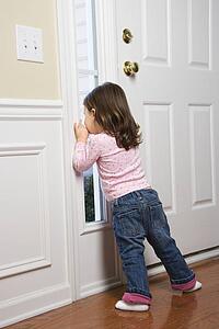 Caucasian girl toddler peeking out of window by door.